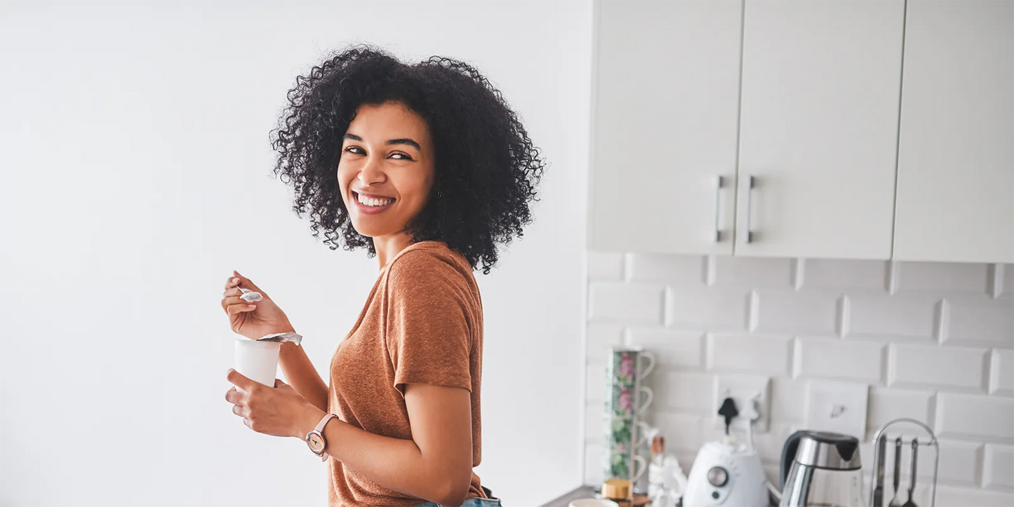 A woman stands in a kitchen, holding a cup of coffee and looking content.